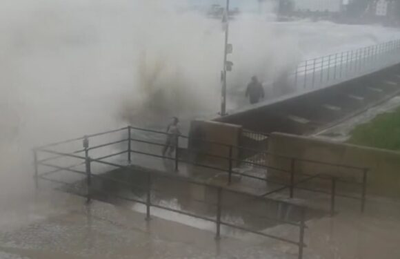 Moment huge waves crash into two children walking with their father