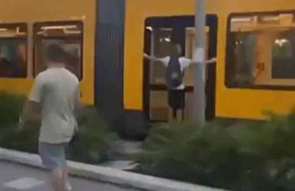 Moment two teens hang dangerously from the side of a tram