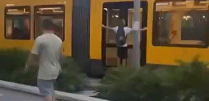 Moment two teens hang dangerously from the side of a tram